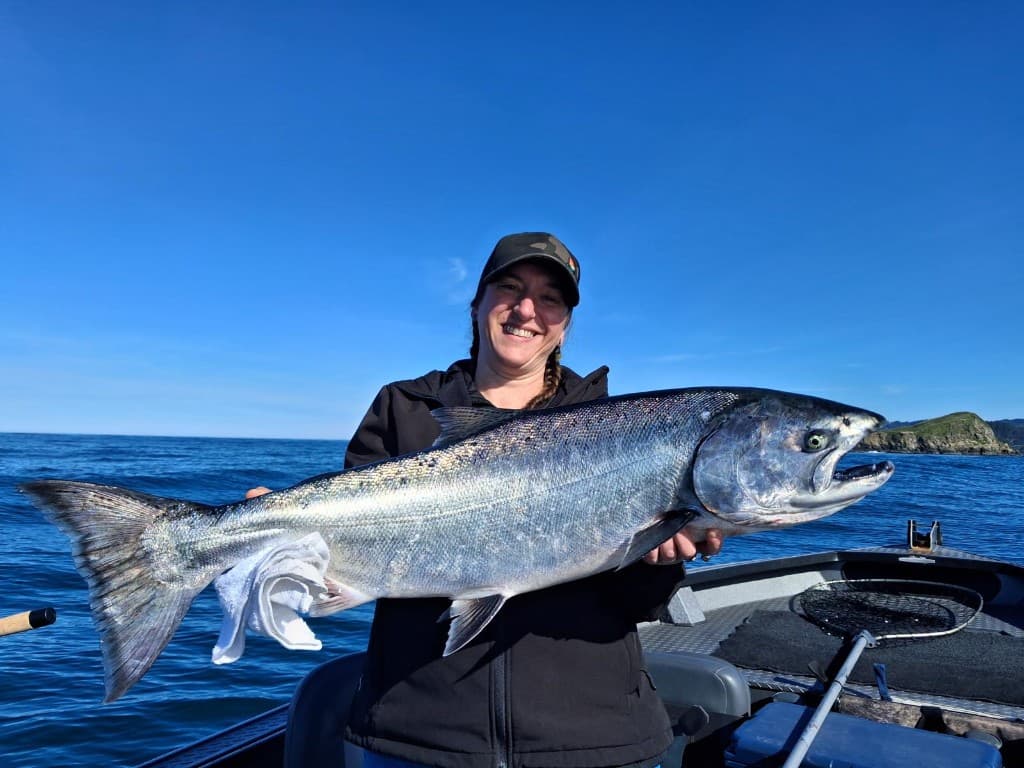 Angler holding a large ocean Chinook salmon on a boat over deep blue water