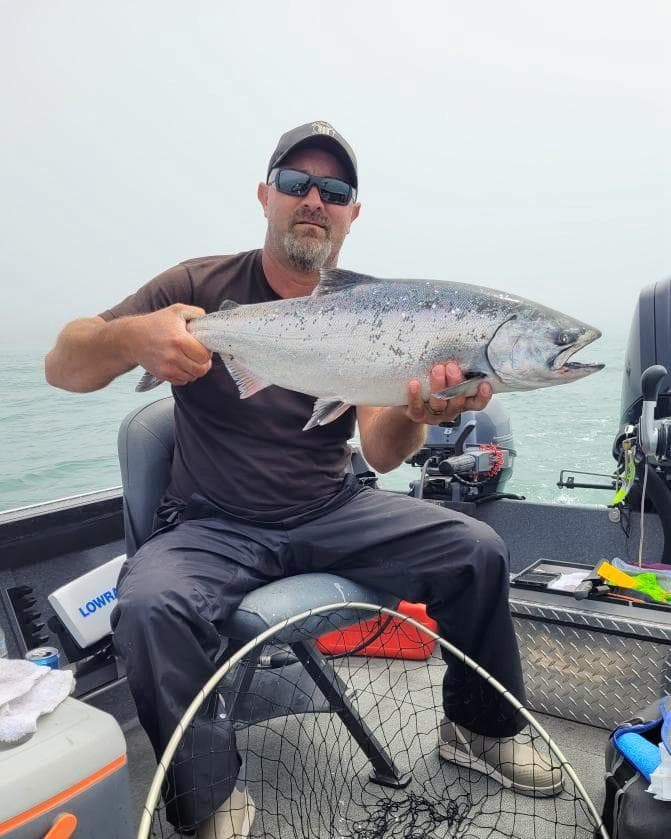 Angler on a boat holding a bright Chinook salmon on a foggy morning at the coast