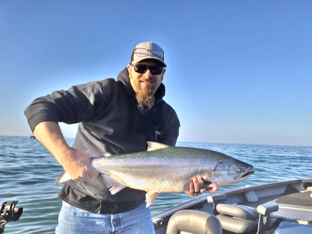 Angler on a drift boat holding a bright Chinook salmon over calm blue water