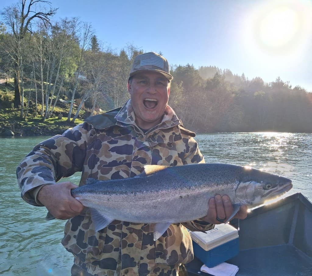 Angler holding a bright Chinook salmon on a sunlit Southern Oregon river