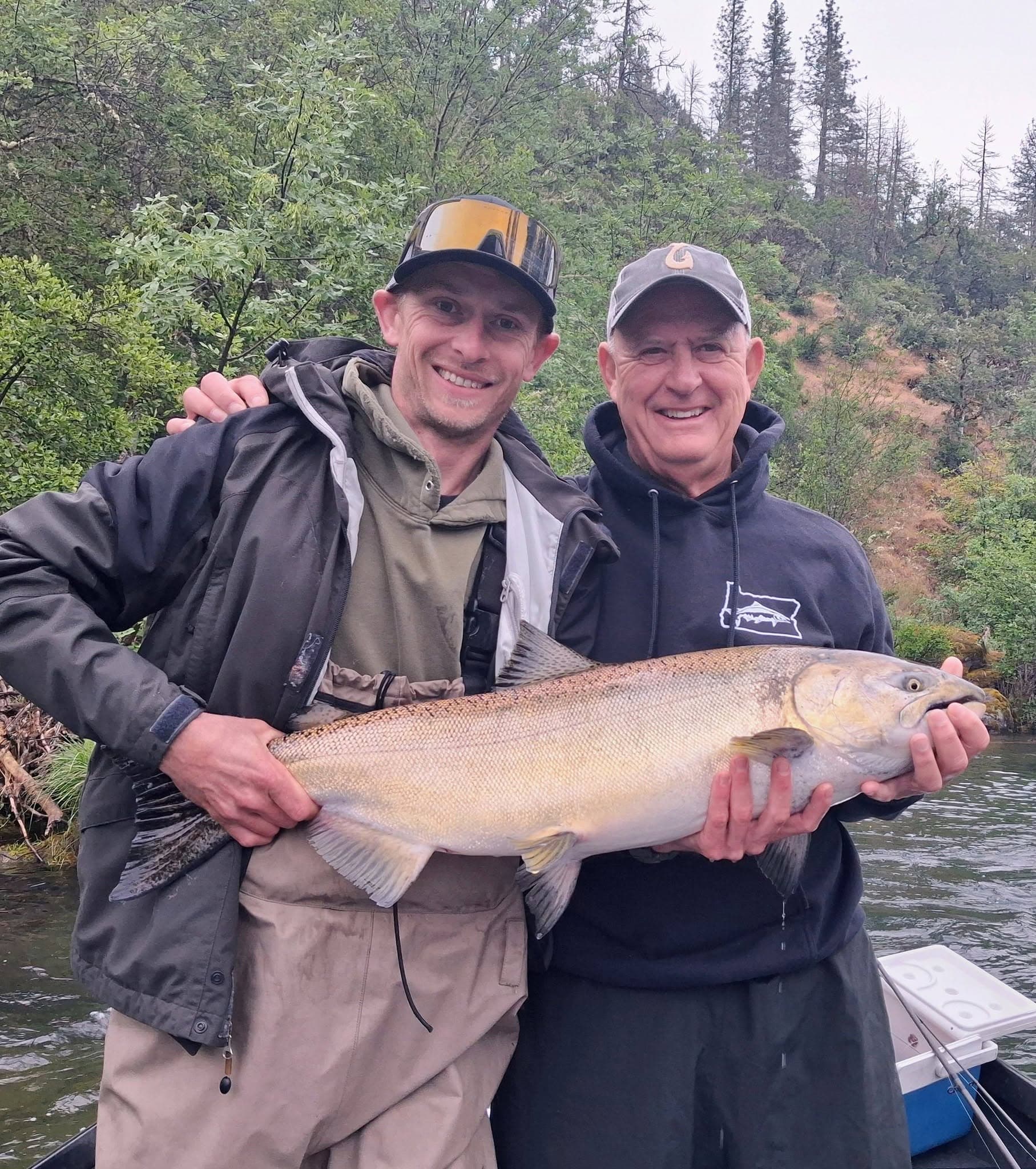 Two anglers holding a salmon on the river surrounded by green forest